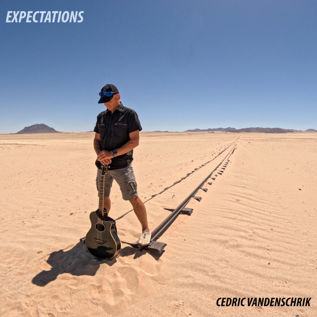 Person standing in the desert at the end of an old railway line with guitar. With writing: Expectations Cedric Vandenschrik